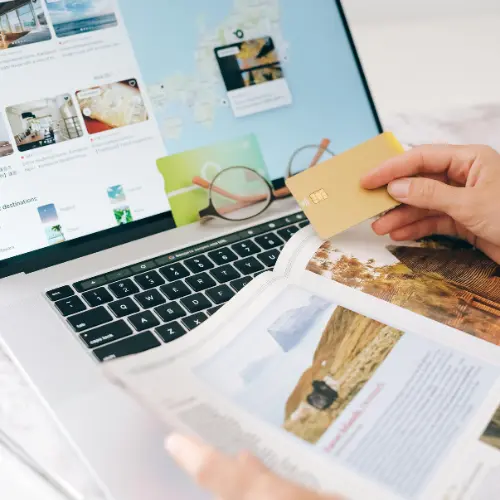 Person using a laptop surrounded by printed documents and holding a credit card